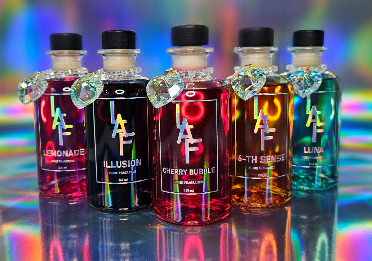 Five bottles of a colorful diffusers with visible brand names on a reflective surface with rainbow background